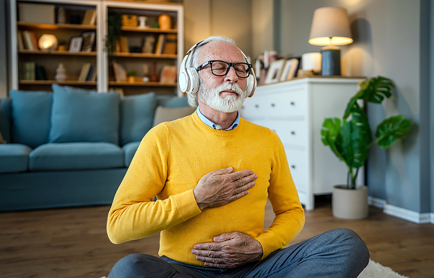 A senior man meditating at home with headphones on.