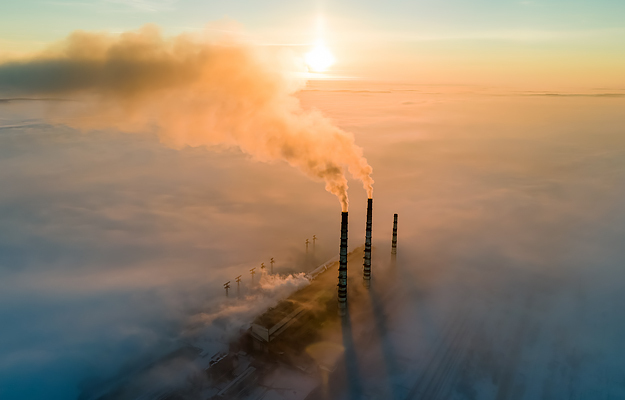 An aerial view of a coal power plant with a dark smoke at sunset.