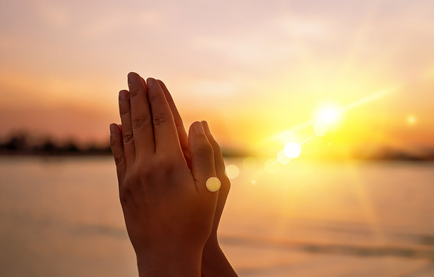 Praying hands with a sunset in the background.