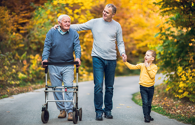 A senior man taking a walk in the park with his adult son and and grandson.