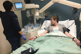 A medical technician watches the monitor of a woman with IVs in a hospital bed.