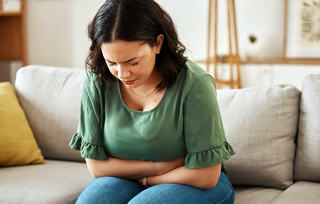 A woman sitting on a couch and holding her stomach.