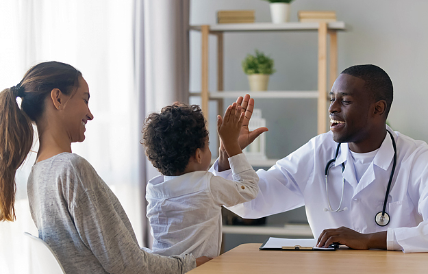 A doctor high fiving a young boy sitting on his mother's lap.