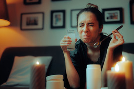 Woman on a couch grimacing at the taste of a drink she has mixed.