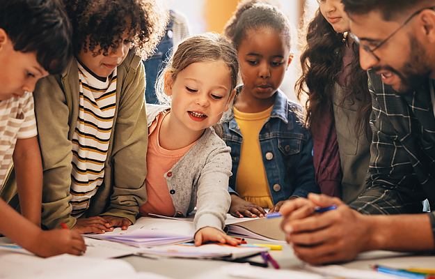 A teacher and small group of elementary school students looking at learning materials together.