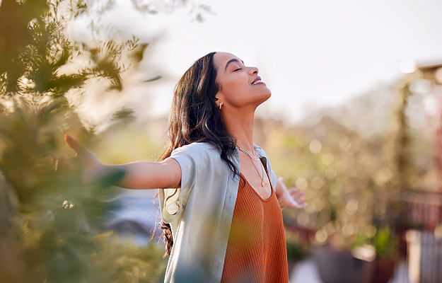 A woman standing outside with her eyes closed and arms outstretched.