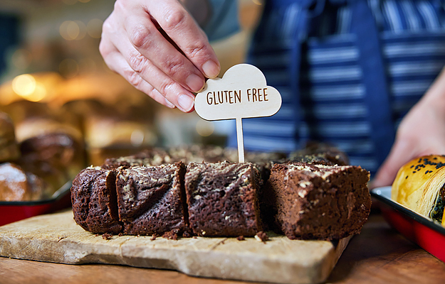A close-up of a bakery employee labeling fresh brownies as gluten free.