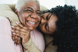 Adult daughter kissing smiling mother.
