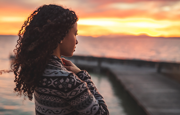 A young woman standing by the water at dusk.