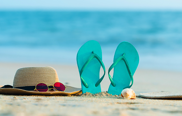 A sun hat, sunglasses, flip flops, and seashell on the beach.