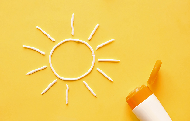 A sun symbol made out of sunscreen next to a tube of sunscreen.