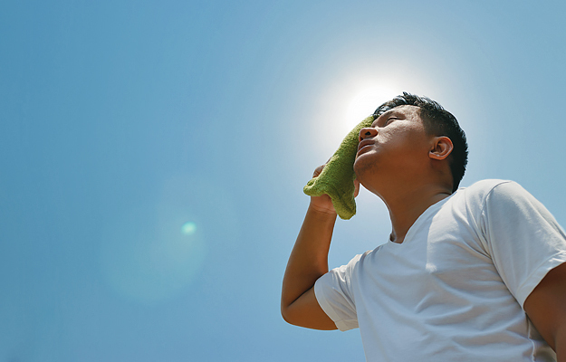 A man wiping sweat off his face with a towel while standing in the sun.