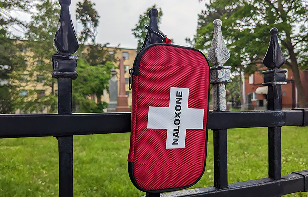 A naloxone kit hanging from a park fence.