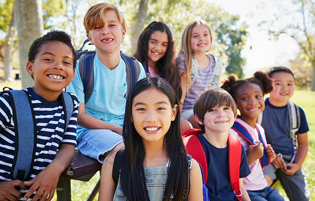 A group of schoolchildren wearing backpacks and posing together outside.