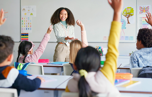 A teacher calling on students with their hands up in a classroom.