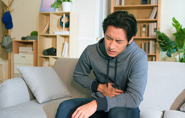 A man sitting on a couch and holding his stomach in pain.