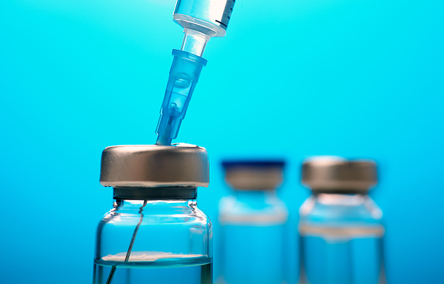 A needle inside of a vaccine vial in the forefront with two vials in the background.