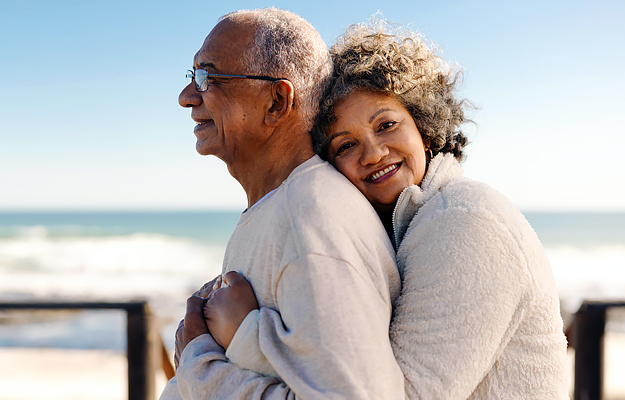 A senior woman embracing her husband by the beach.