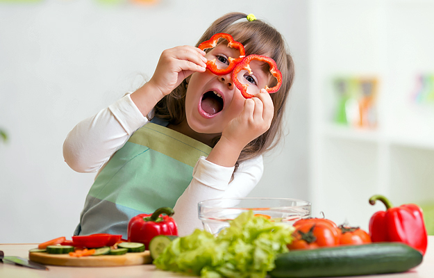 A young girl having fun in the kitchen while preparing vegetables.