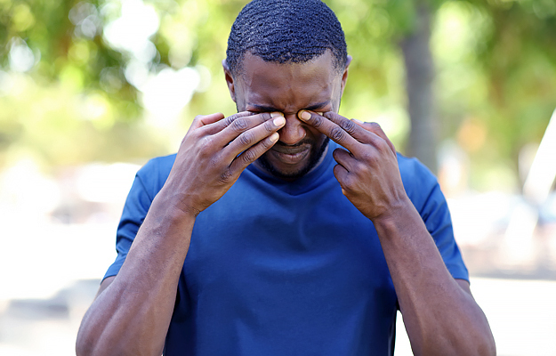 A man standing outside and rubbing his eyes.