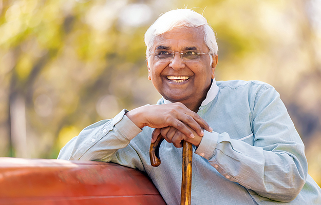 A smiling senior man sitting on a park bench with a cane.