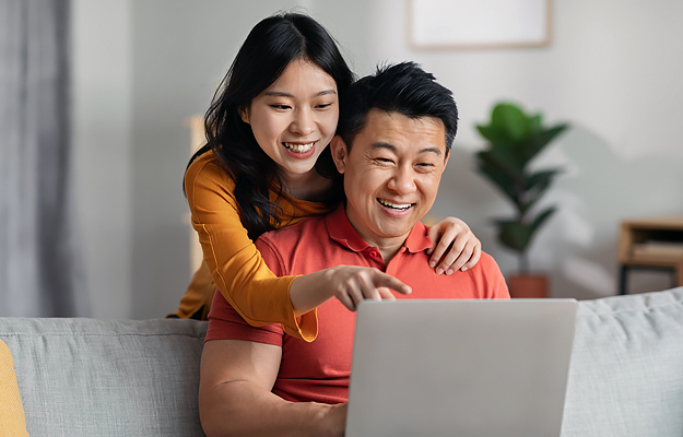 A smiling Asian couple looking at a laptop together.