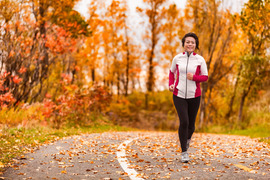 Middle-age Asian woman running on a park path through autumn foliage.