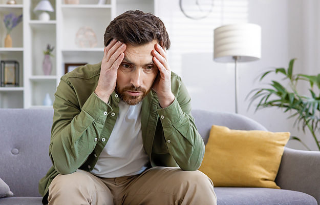 A man sitting on a couch and holding his head out of frustration.