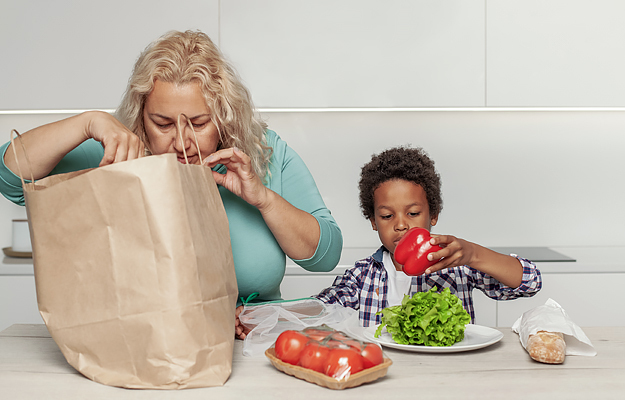 A mother and her young son taking healthy groceries out of a paper shopping bag.