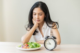 Young woman gazing at a salad beside an alarm clock showing 10:45.