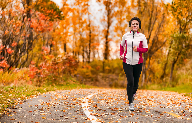 A woman running on a park path through autumn foliage.