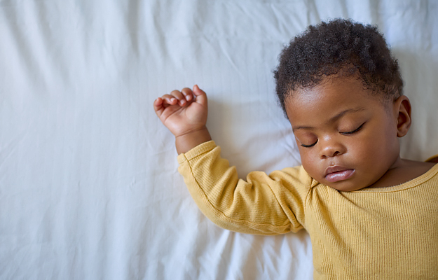 A baby sleeping on her back on top of a fitted sheet.