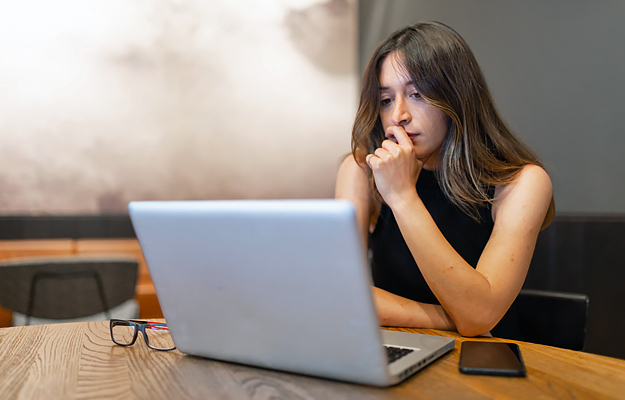 A pensive woman looking at a laptop.