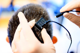 Researcher plugging a cable into a device on a person’s head.