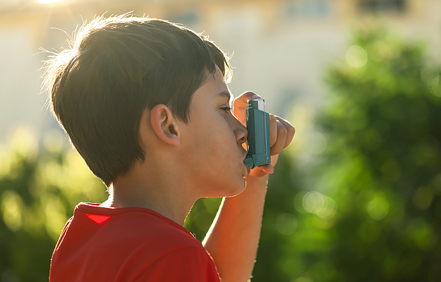 A young boy using an inhaler outside.