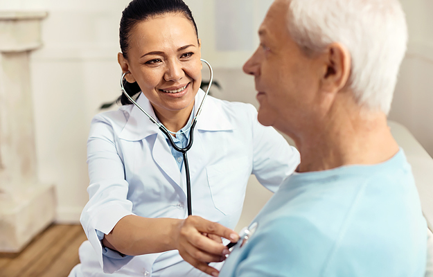 A female doctor listening to a senior male patient's heart with a stethoscope.