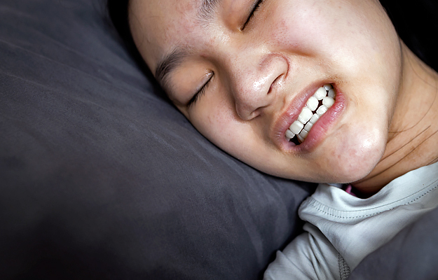 A young girl lying in bed and suffering from bruxism.
