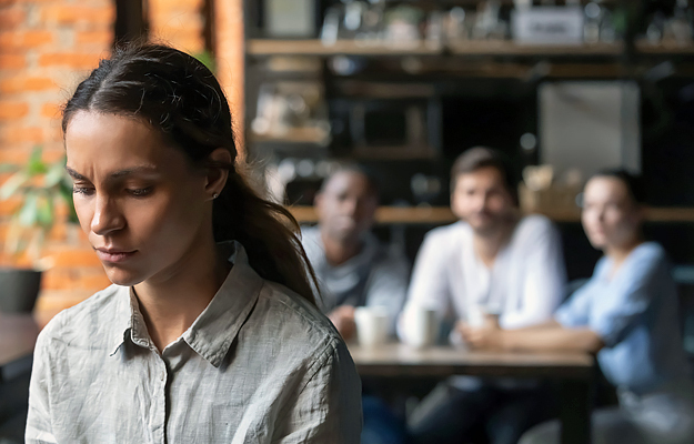 An upset young woman sitting alone with three friends in the background.