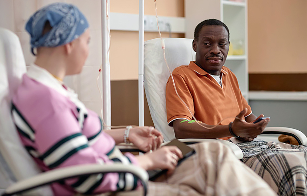 A man talking to a woman wearing a headscarf during chemotherapy treatment in a clinic.