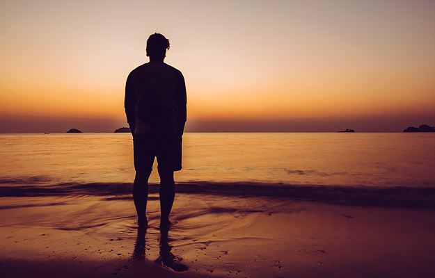 A silhouette of a man standing on the beach at sunset.
