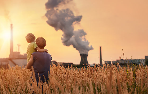 A father holding his son while looking at a smokestack in the distance.