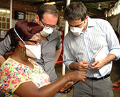 Researchers wearing surgical masks collaborate around a mobile device using the electronic mobile comprehensive health application (emocha).