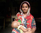 Woman seated indoors breastfeeds a baby.