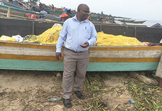 Dr. Joseph K.B. Matovu stands in front of a fishing boat on the shoreline in Uganda