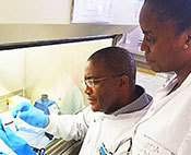 Dr. Moyo Sikhulile and a colleague dressed in lab coats work with sample in the lab