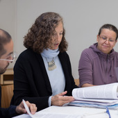 Dr. Florencia Luna (center) is seated at a table talking with trainees.