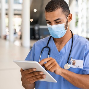 Person in blue scrubs with a facemask using a tablet computer