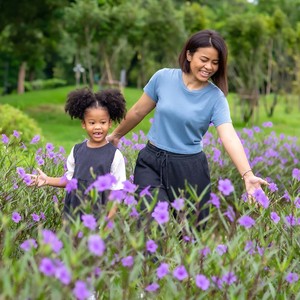 Happy mixed race mother with little daughter holding hands and walking together in the garden.