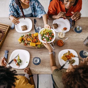 Unrecognizable female friends sitting in the dining room and eating vegetarian food together