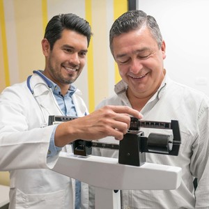 Doctor checking the weight of a mid adult male patient both smiling very happy